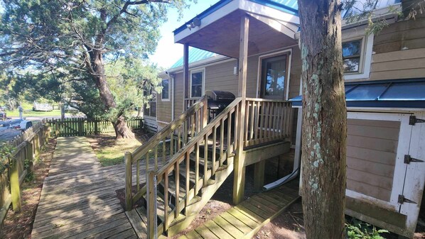 A wooden deck leading to a house with a covered porch and a grill. - Happy Place: Pet friendly, fenced rear yard with deck. (Ocracoke)