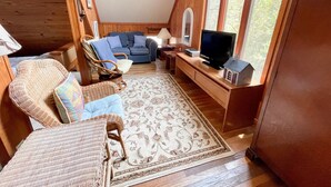 A cozy, wooden-furnished living room with a sofa, chairs, a television, and a patterned rug. - Happy Place:  Pet friendly, fenced rear yard with deck. (Ocracoke)