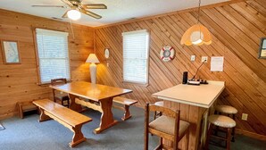 Una habitación con interior de madera, un ventilador de techo, una mesa con bancos y una pequeña zona de bar con taburetes.