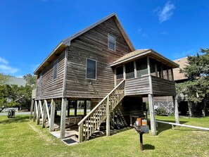 A two-story wooden house with a porch and a staircase leading to the upper level.