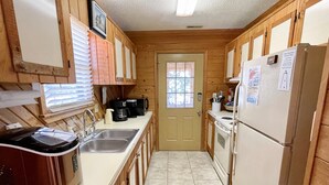 Una cocina compacta con armarios de madera, un lavamanos de acero inoxidable, una cafetera y un refrigerador.
