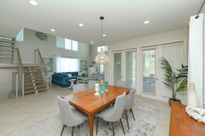 A spacious living area with a wooden dining table, grey chairs, and a hanging light fixture.
