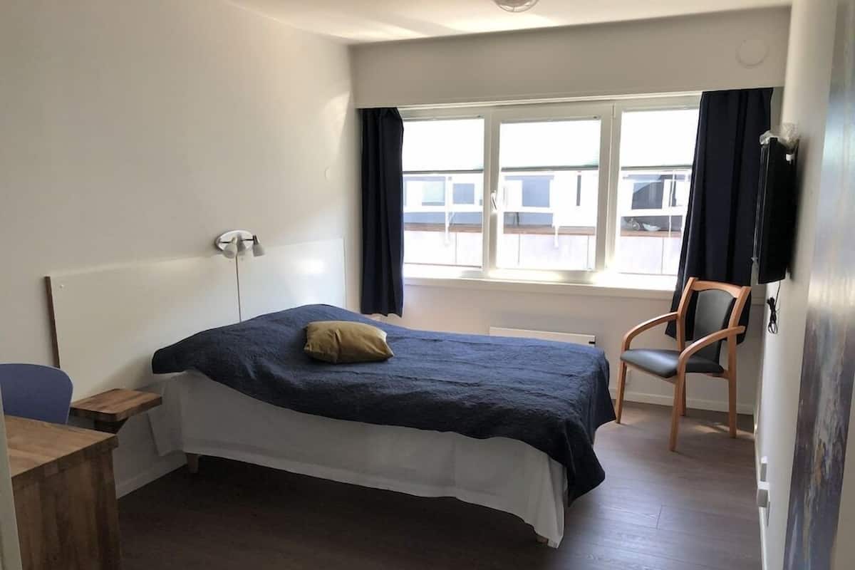A bedroom with a bed, a chair, a desk, and a window with curtains.