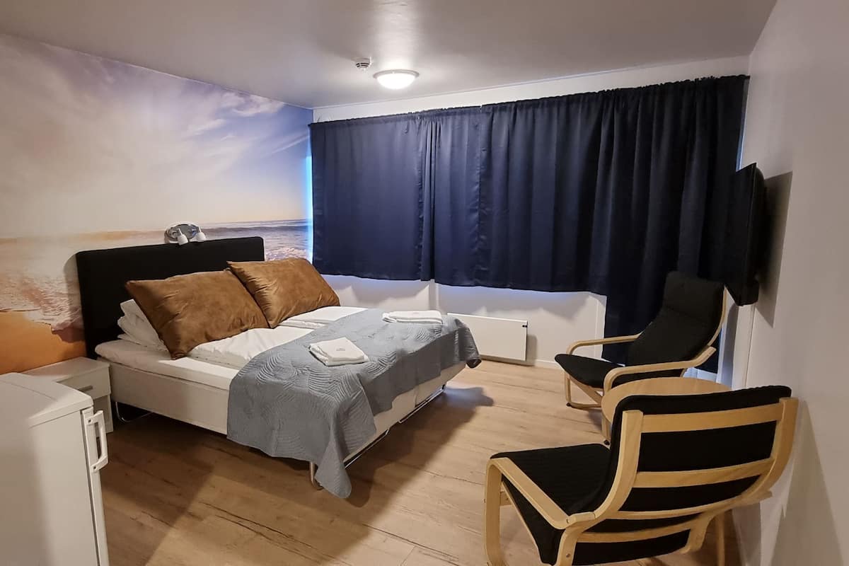 A bedroom with a bed, a desk, a chair, a TV, and a wall with a painted landscape.