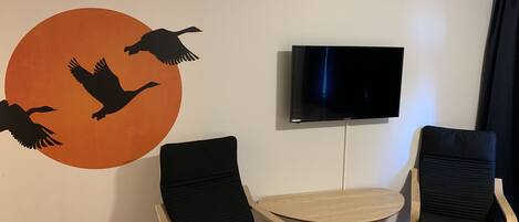 A room with two black chairs, a small round table, a TV mounted on the wall, and a wall decal of birds flying.