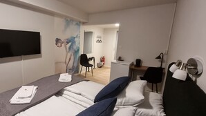Habitación de hotel con cama, escritorio, silla, televisor y un cuadro en la pared.
