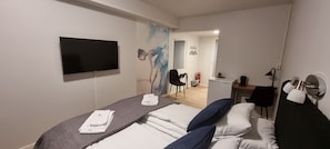 A hotel room with a bed, a desk, a chair, a TV, and a painting on the wall.