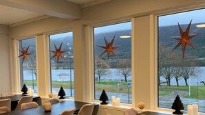 A conference room with large windows, star decorations, and a view of a lake and mountains. - Husnes Sentrum Hotell (Kvinnherad)
