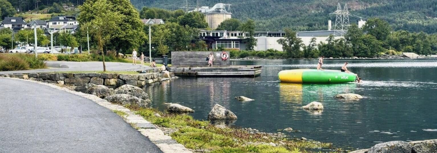 Un lac avec un quai, un radeau gonflable vert et jaune, et un mur de pierres le long de la rive.