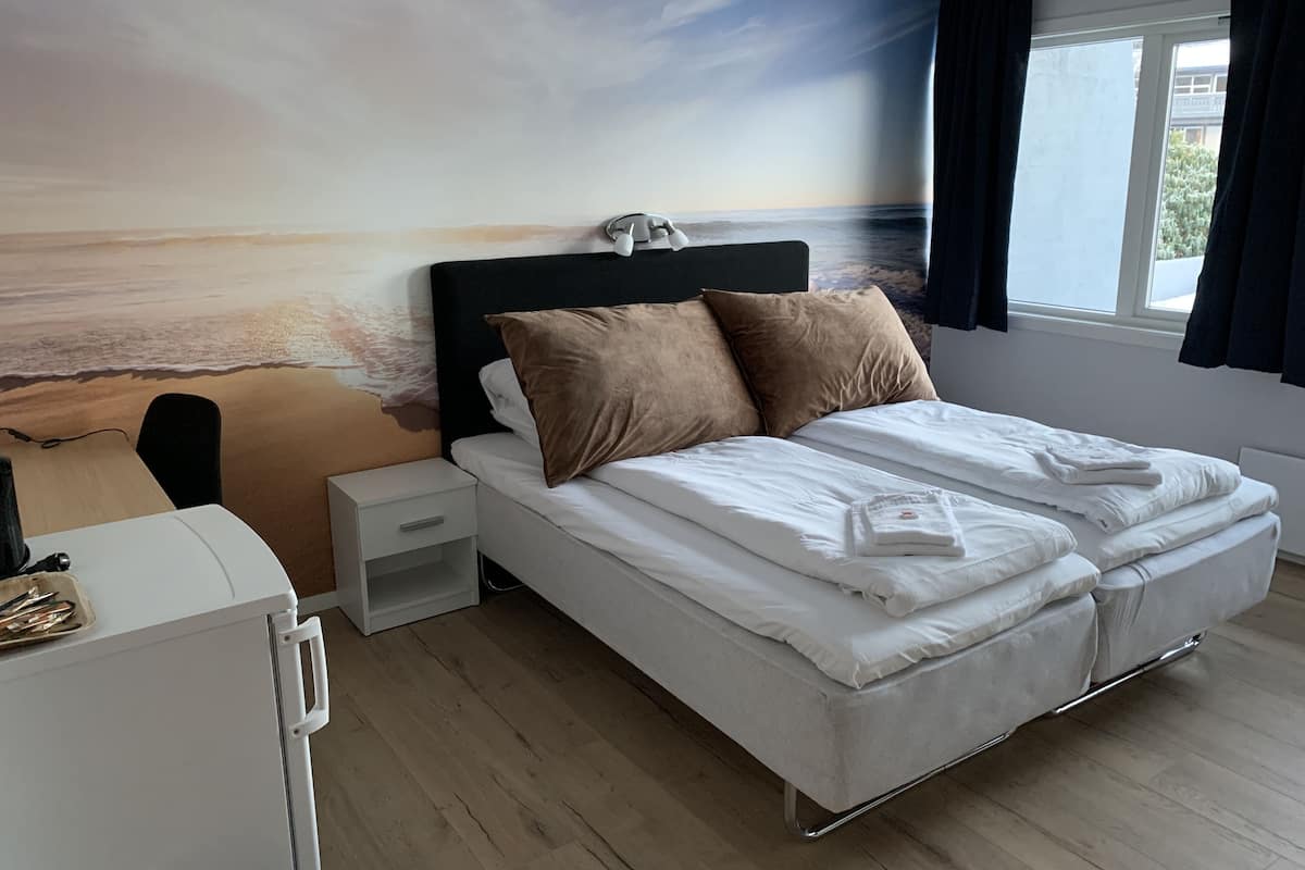 A bedroom with a bed, bedside tables, a desk, and a large wall mural of a beach scene.
