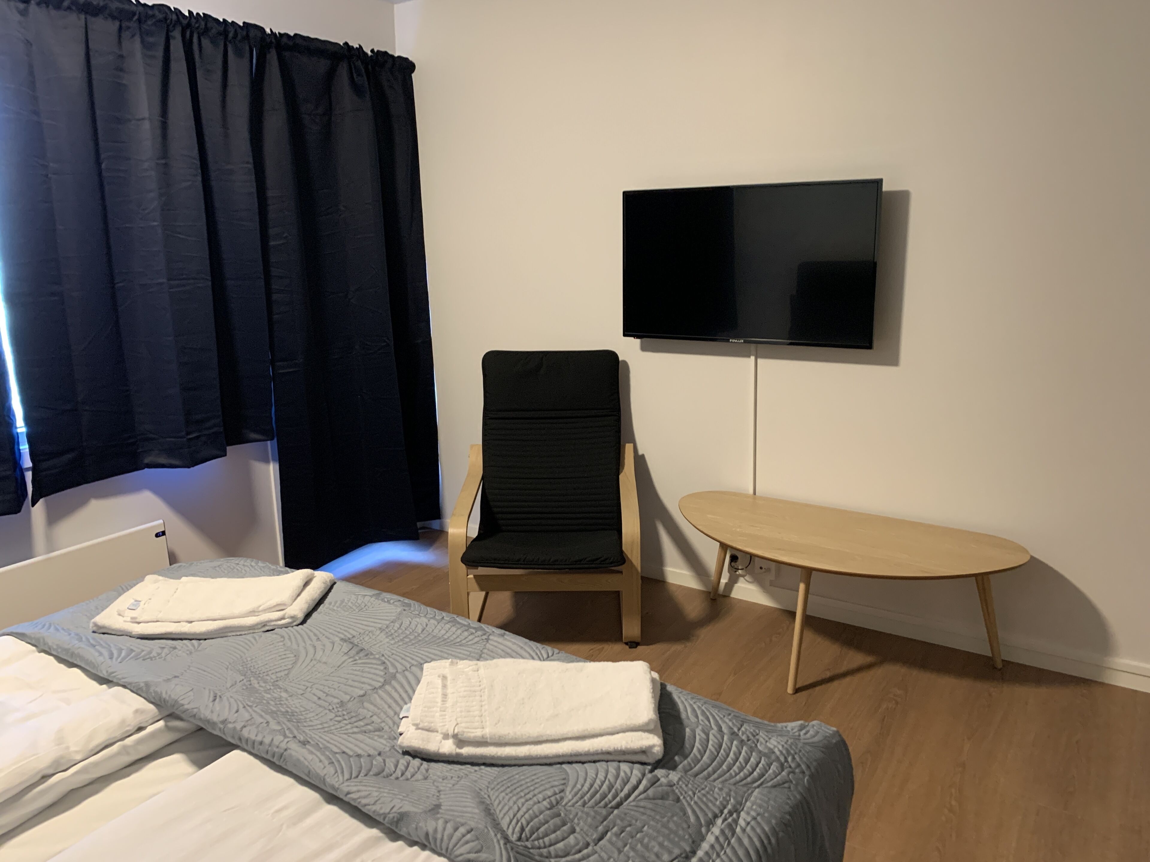 A hotel room with a bed, a chair, a small table, and a TV mounted on the wall.