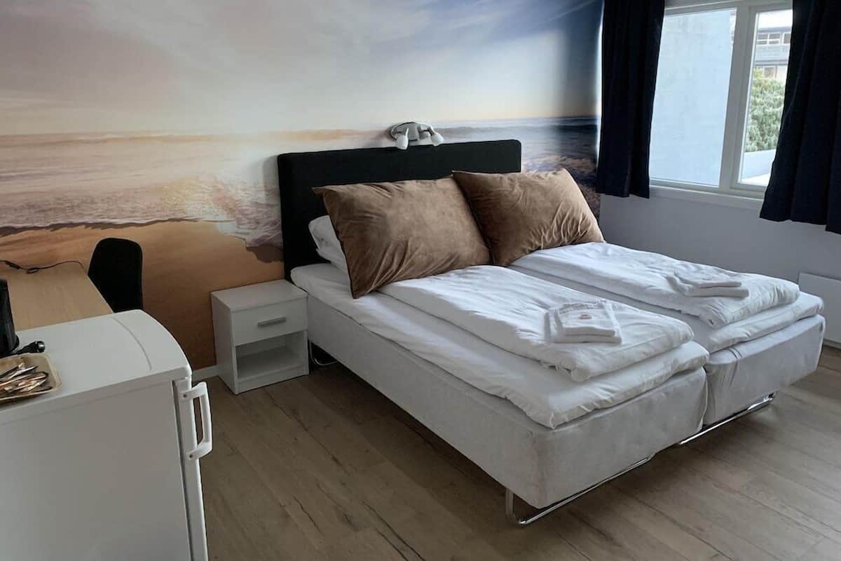 A bedroom with a bed, a nightstand, a desk, and a window with curtains.