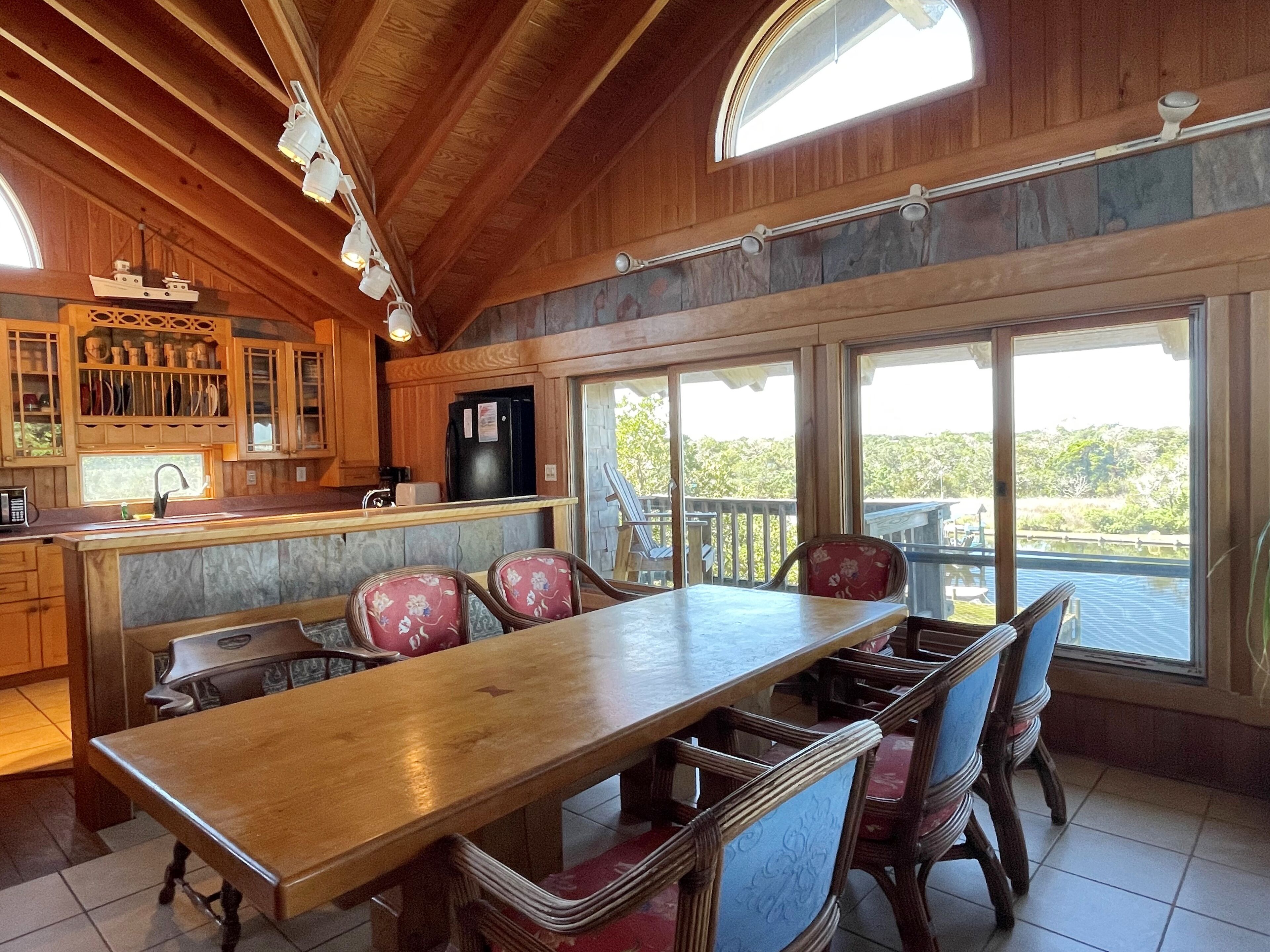 A wooden interior with a kitchen, dining area, and large windows offering a view of the outdoors.