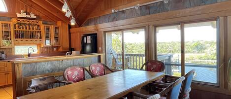 A wooden interior with a kitchen, dining area, and large windows offering a view of the outdoors.
