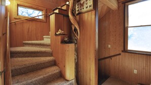 A wooden staircase with a unique spiral design, carpeted steps, and a small window at the top. - Cuttin' Sage:  Tropical flavor, reverse floorplan, canal, marsh views. (Ocracoke)