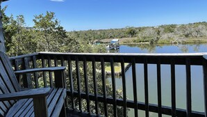 A wooden deck with a view of a calm lake, surrounded by trees and a distant hill. - Cuttin' Sage:  Tropical flavor, reverse floorplan, canal, marsh views. (Ocracoke)