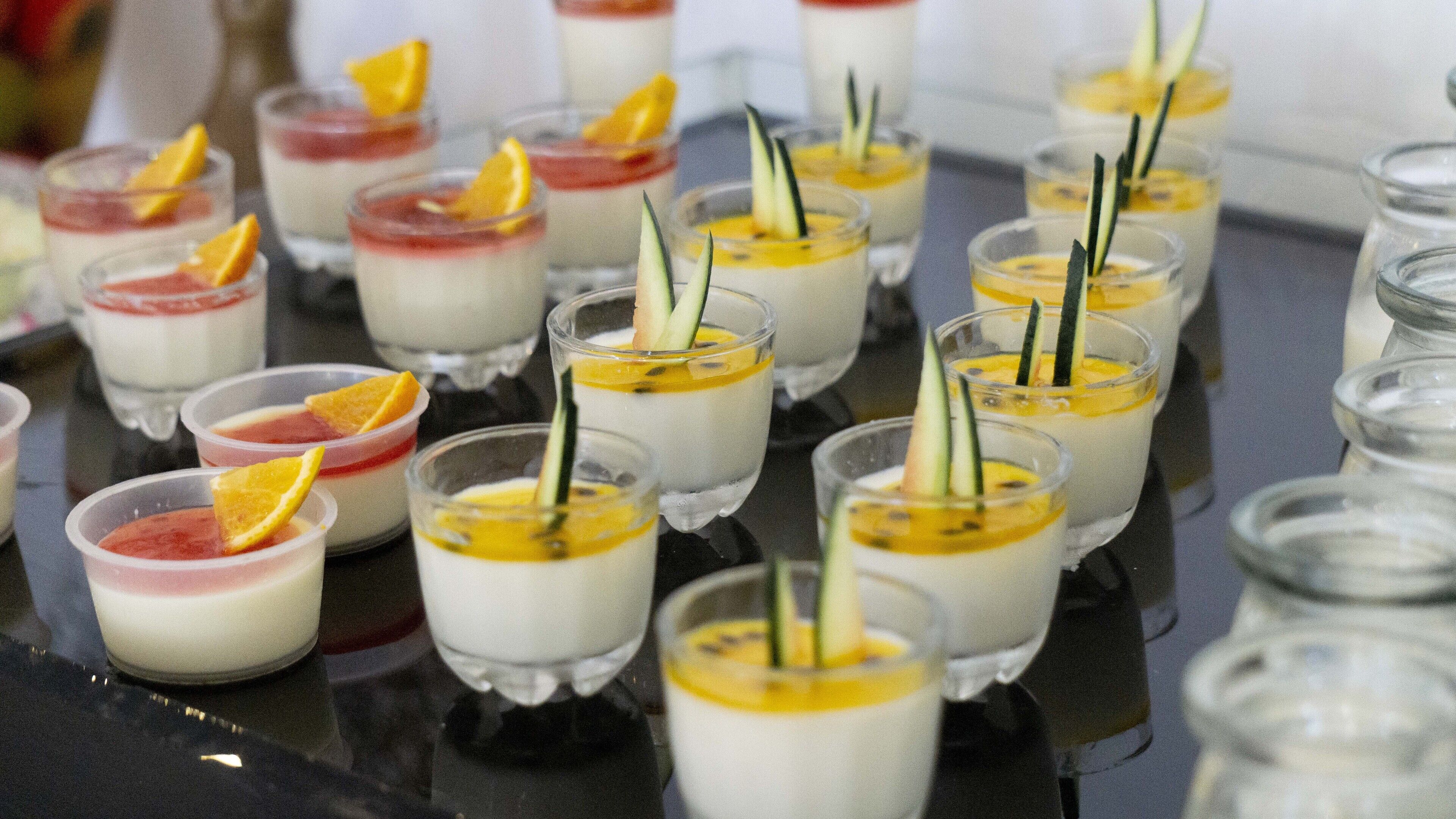 A variety of small dessert cups arranged on a reflective surface.