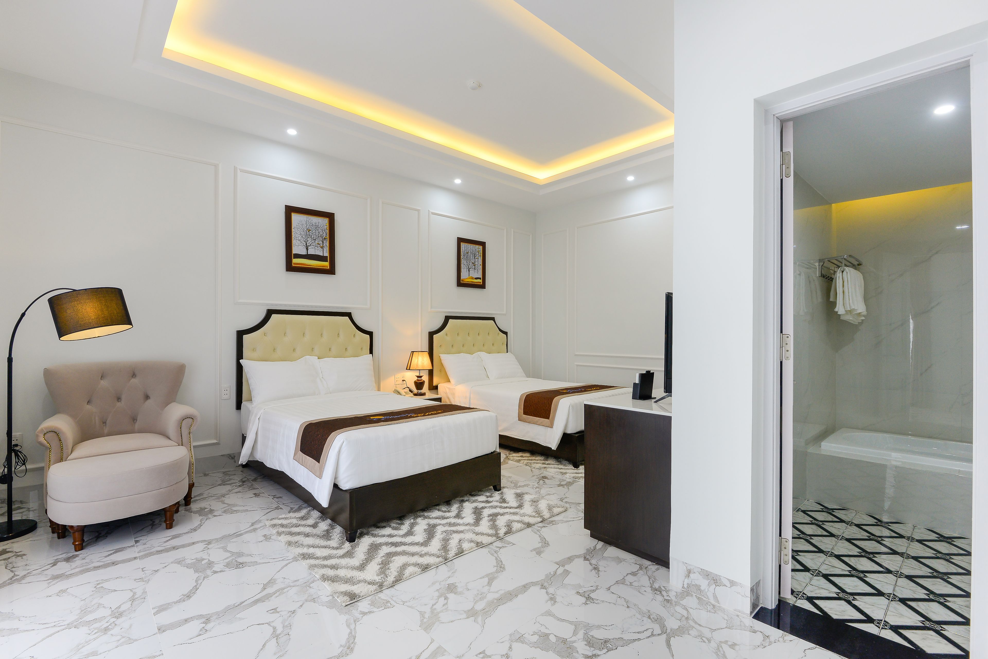 A hotel room with two beds, a sofa, a desk, a lamp, and a shower area.