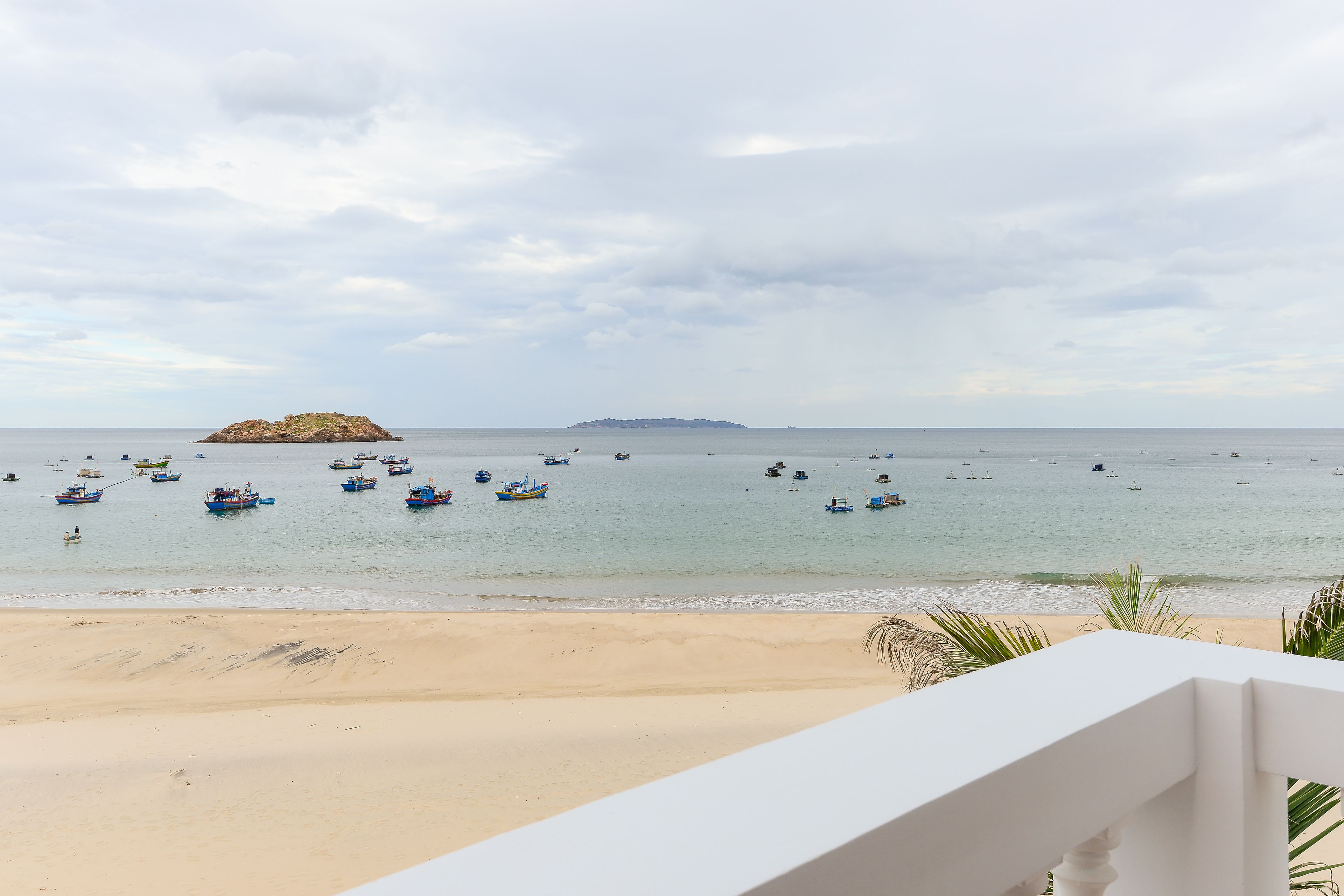A beach with boats in the water and a distant island.
