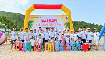 Eine Gruppe von Menschen posiert vor einem bunten, aufblasbaren Bogen mit einem Banner, auf dem steht: TEAM BUILDING ONE TEAM ONE DREAM.