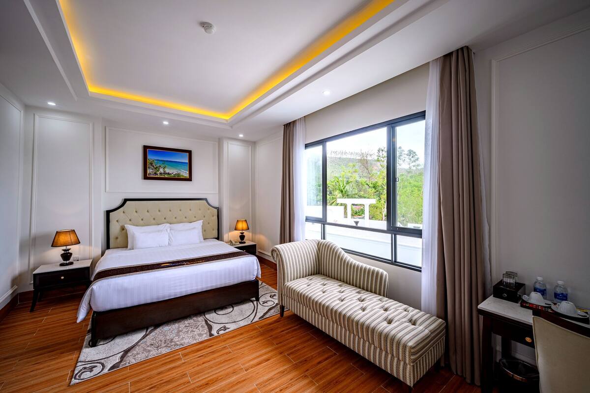Ein Hotelzimmer mit Bett, Nachttischen, einer Couch, einem Fenster mit Aussicht und einem Schreibtisch mit Stuhl.