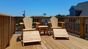Une terrasse en bois avec deux fauteuils Adirondack et une petite table, le tout entouré d’une balustrade en bois.