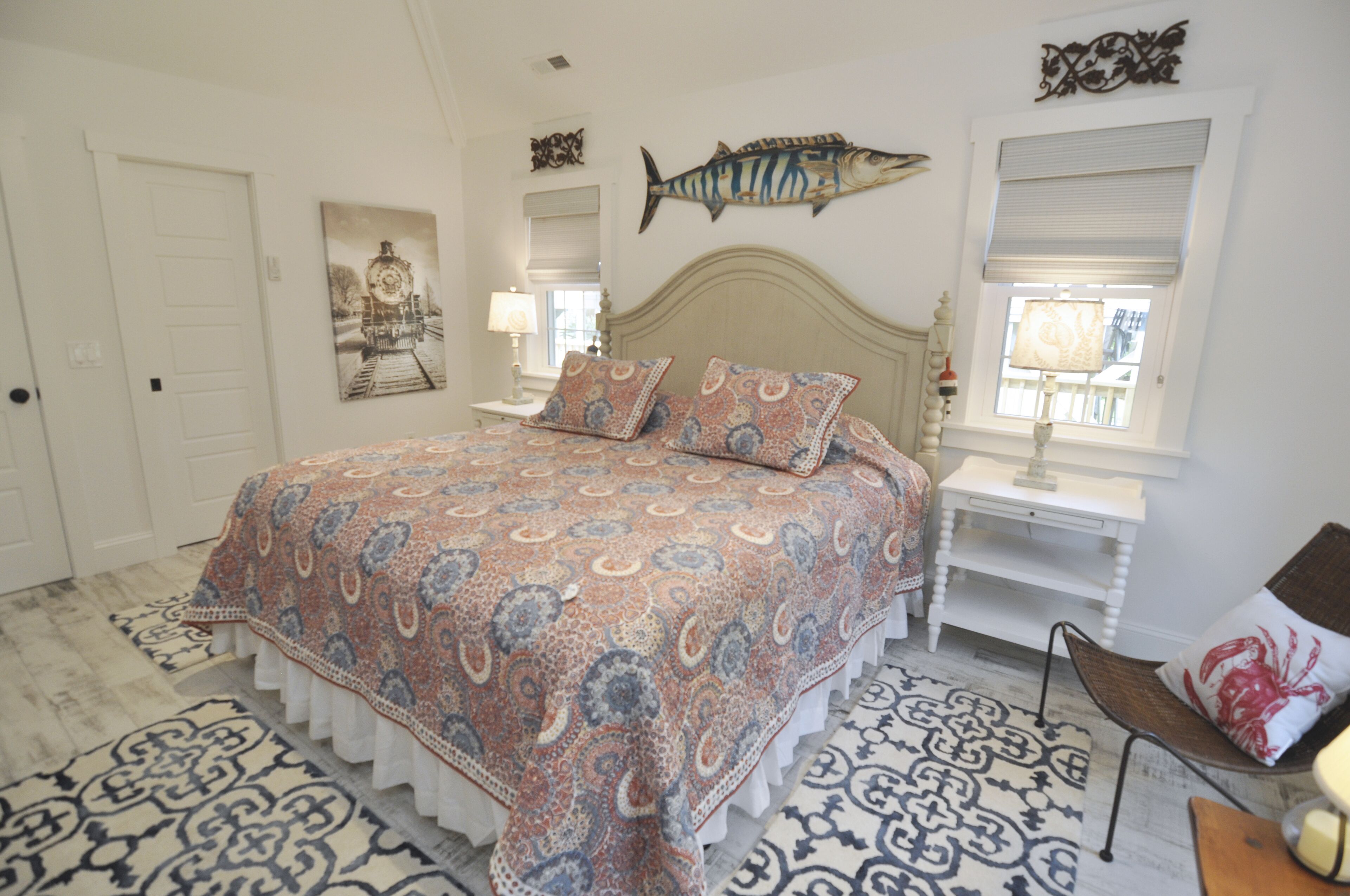 Une chambre avec un grand lit, une couvre-lit à motifs, une décoration murale représentant des poissons, une chaise et une fenêtre donnant sur un beau paysage.