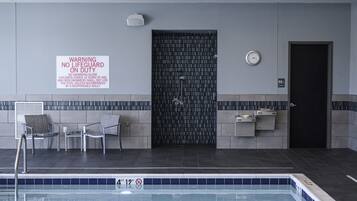 Une zone autour d’une piscine, avec un panneau d’avertissement indiquant la présence d’un sauveteur, une porte et une horloge au mur.