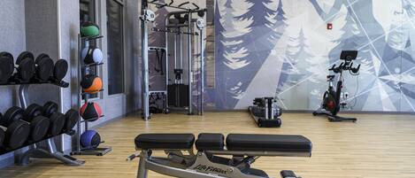A gym with weightlifting equipment, exercise balls, and a wall mural.