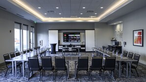 A conference room with a long table, chairs, and a large screen at the front. - Hyatt House Indianapolis / Fishers (Fishers)