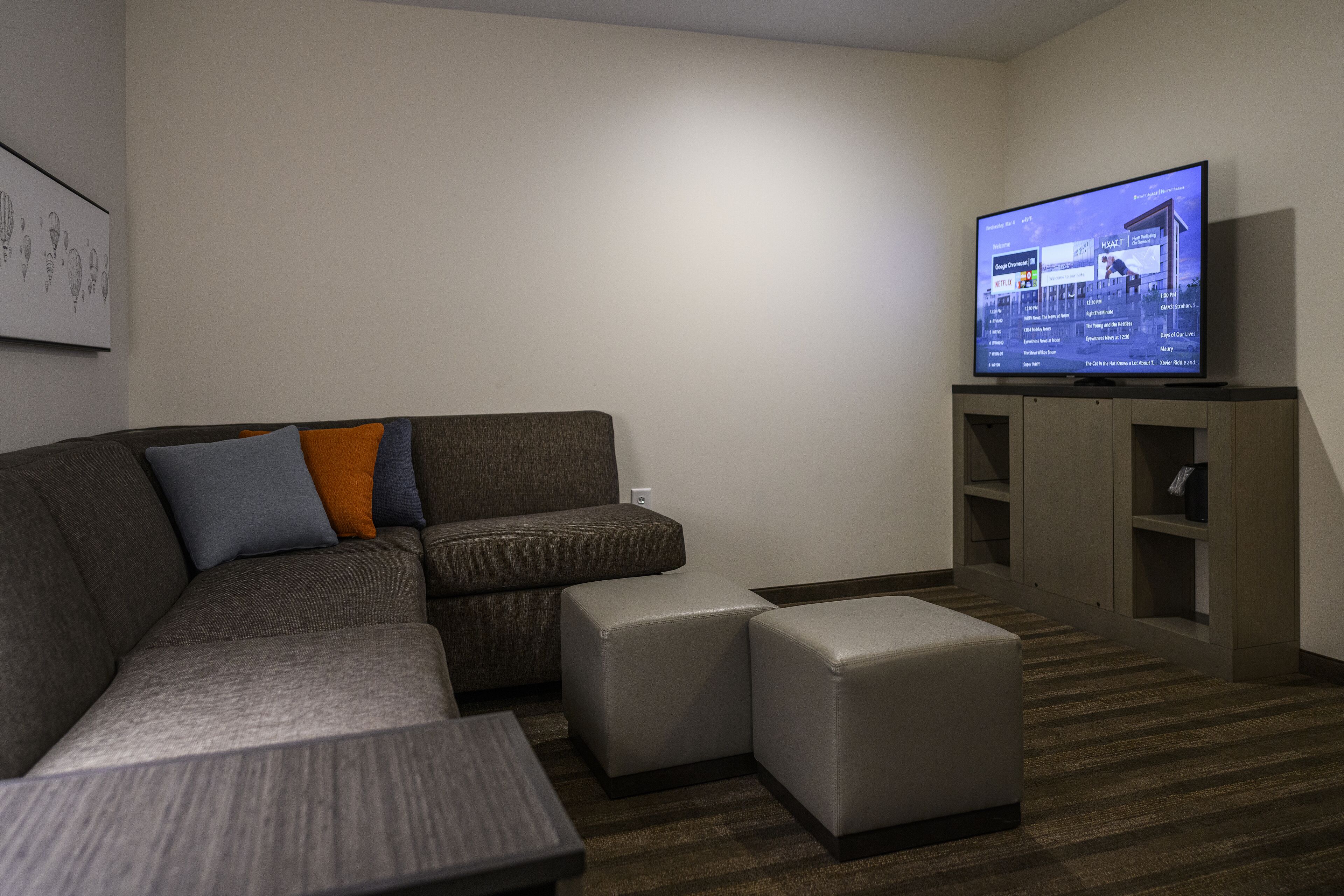 A modern living room with a sectional sofa, ottomans, a flat-screen TV, and built-in shelving.
