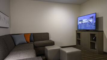 A modern living room with a sectional sofa, ottomans, a flat-screen TV, and built-in shelving.