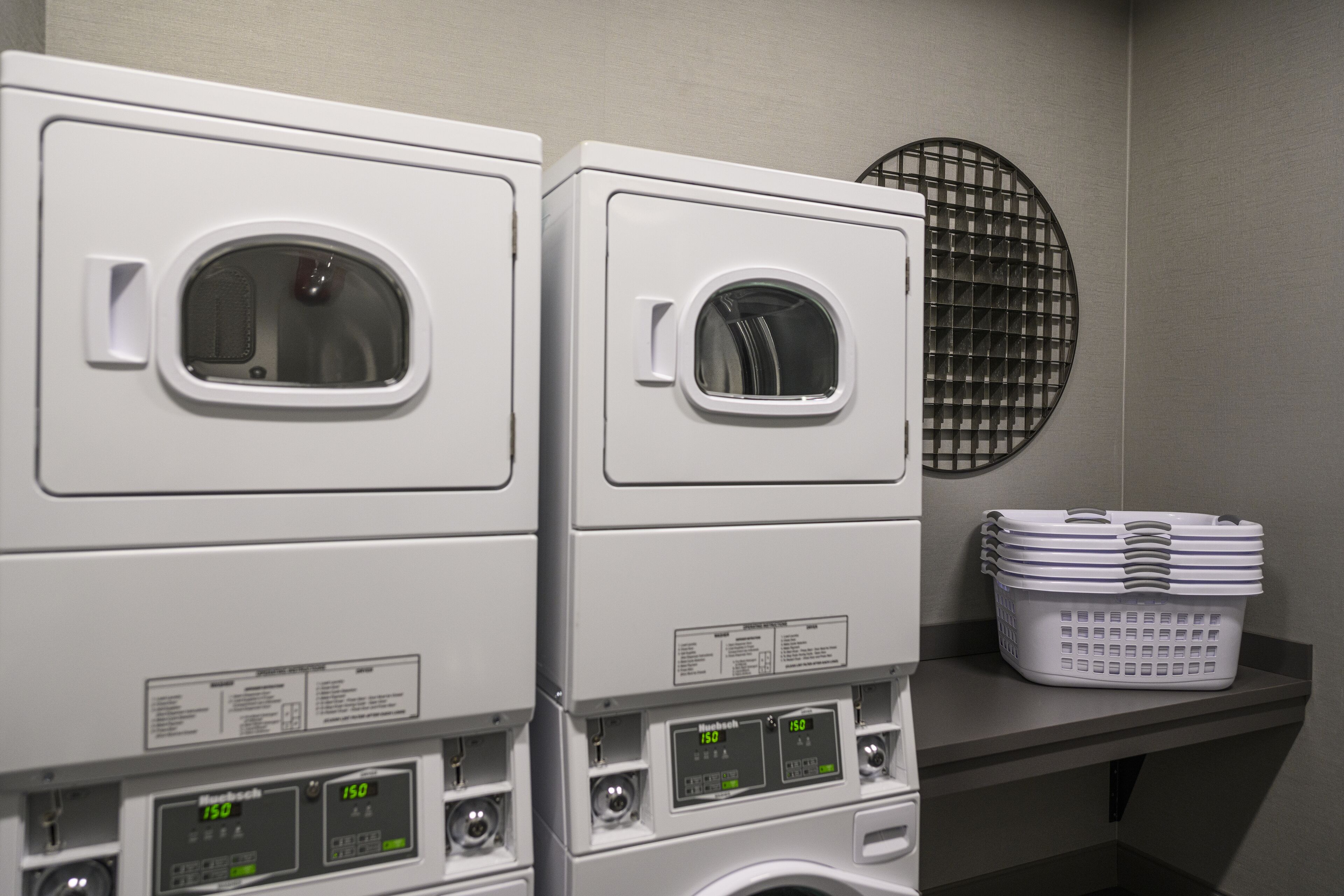 A laundry area with two stacked washing machines and a basket of laundry on a shelf.