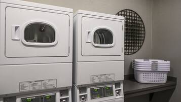 A laundry area with two stacked washing machines and a basket of laundry on a shelf.