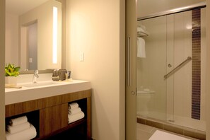 A modern bathroom with a glass-enclosed shower, a sink with a mirror, and a wooden vanity with towels. - Hyatt Place Indianapolis / Fishers (Fishers)