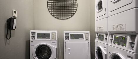 A laundry room with two front-loading washers and dryers, a phone, and a circular vent on the wall.