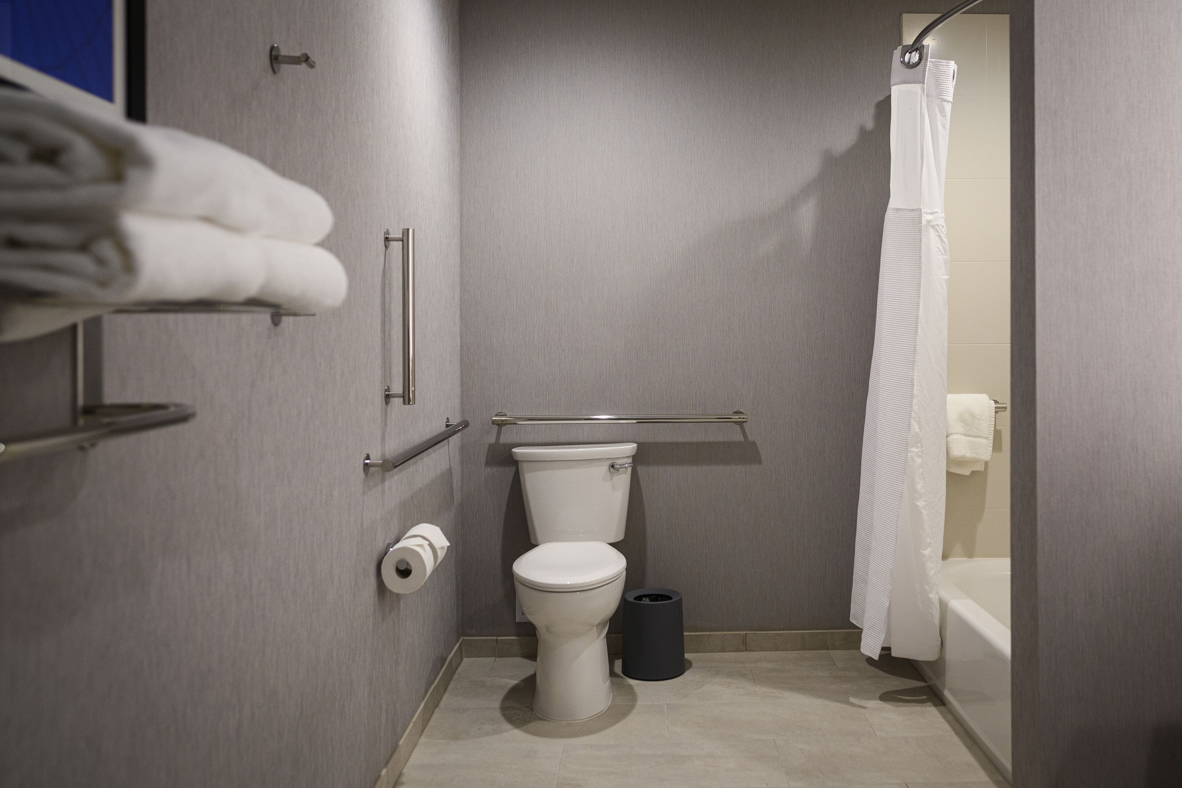 A compact bathroom with a toilet, a trash bin, a towel rack, and a shower curtain.