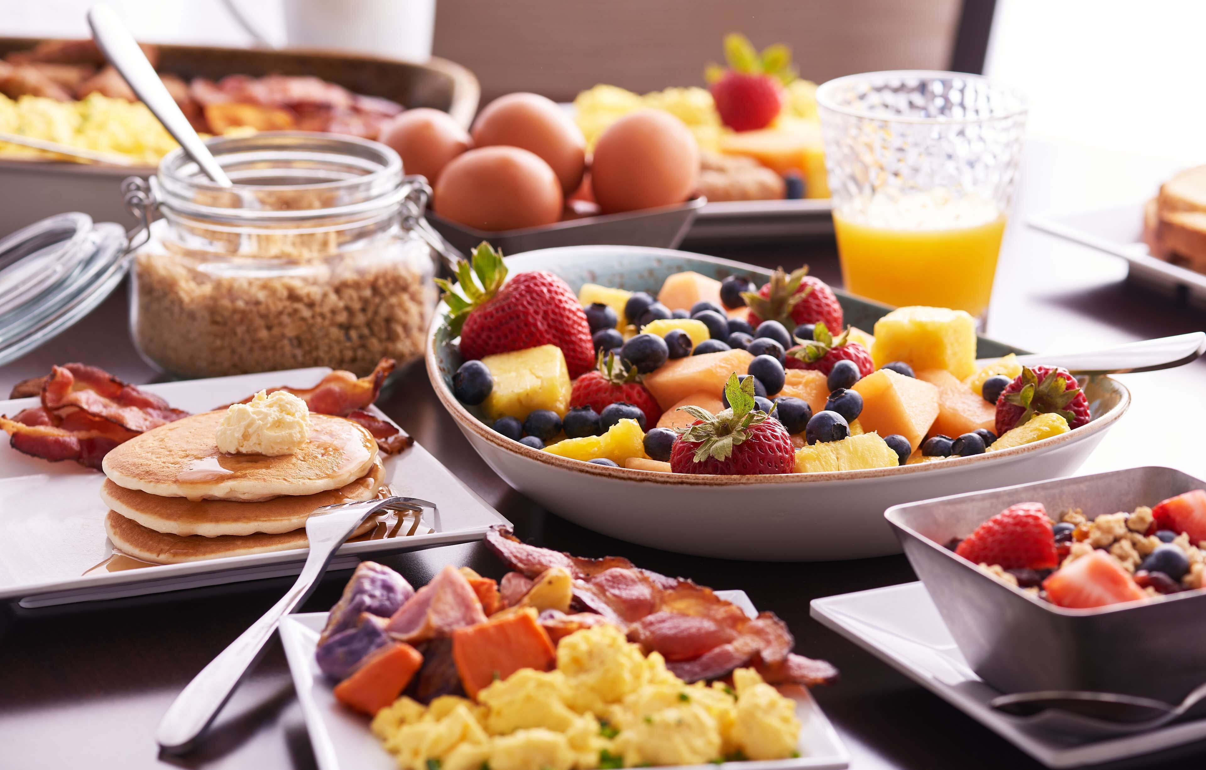 A breakfast buffet with various dishes including pancakes, scrambled eggs, bacon, and a fruit bowl.