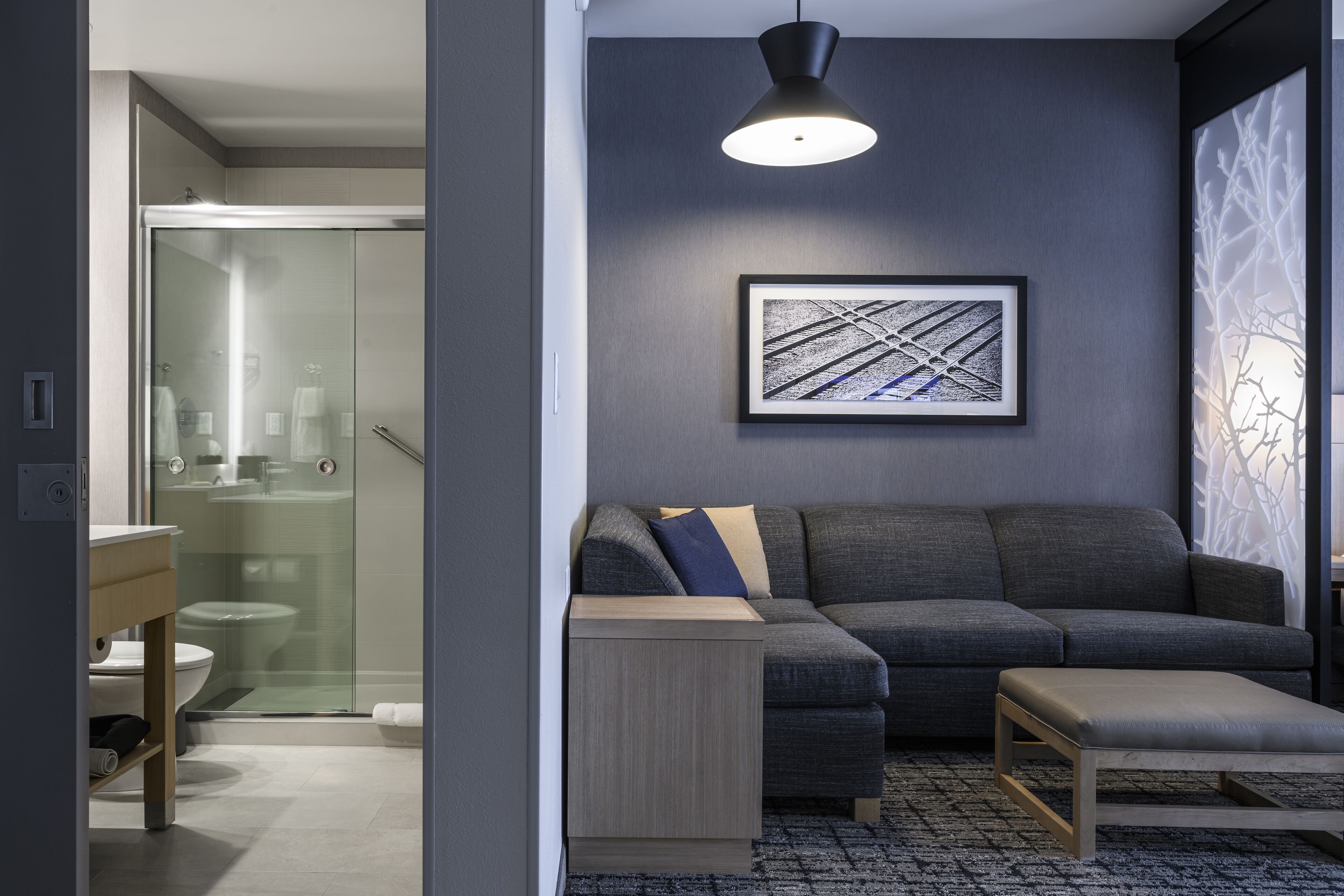 A modern living room with a gray sofa, a small wooden side table, and a framed abstract artwork on the wall.