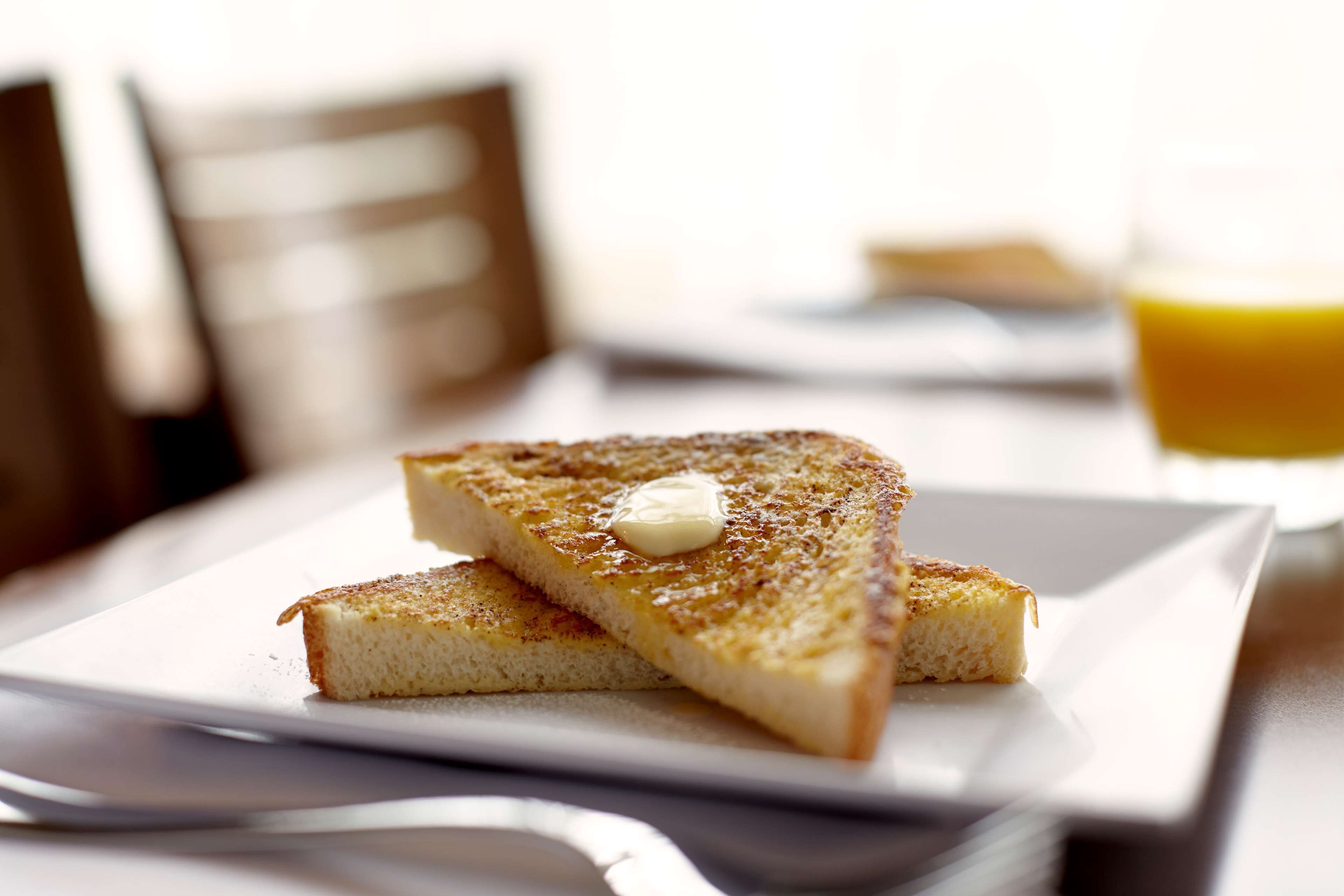 Een ontbijtje met toast en boter, een glas sinaasappelsap en een vork op een tafel.