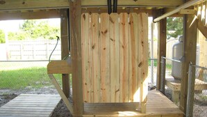 Una struttura in legno con recinzione a listelli, cancello in metallo e una piattaforma in cemento.