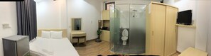 A hotel room with a bed, a desk, a mirror, a wardrobe, and a shower. - Quoc Minh Apartment (Nha Trang)