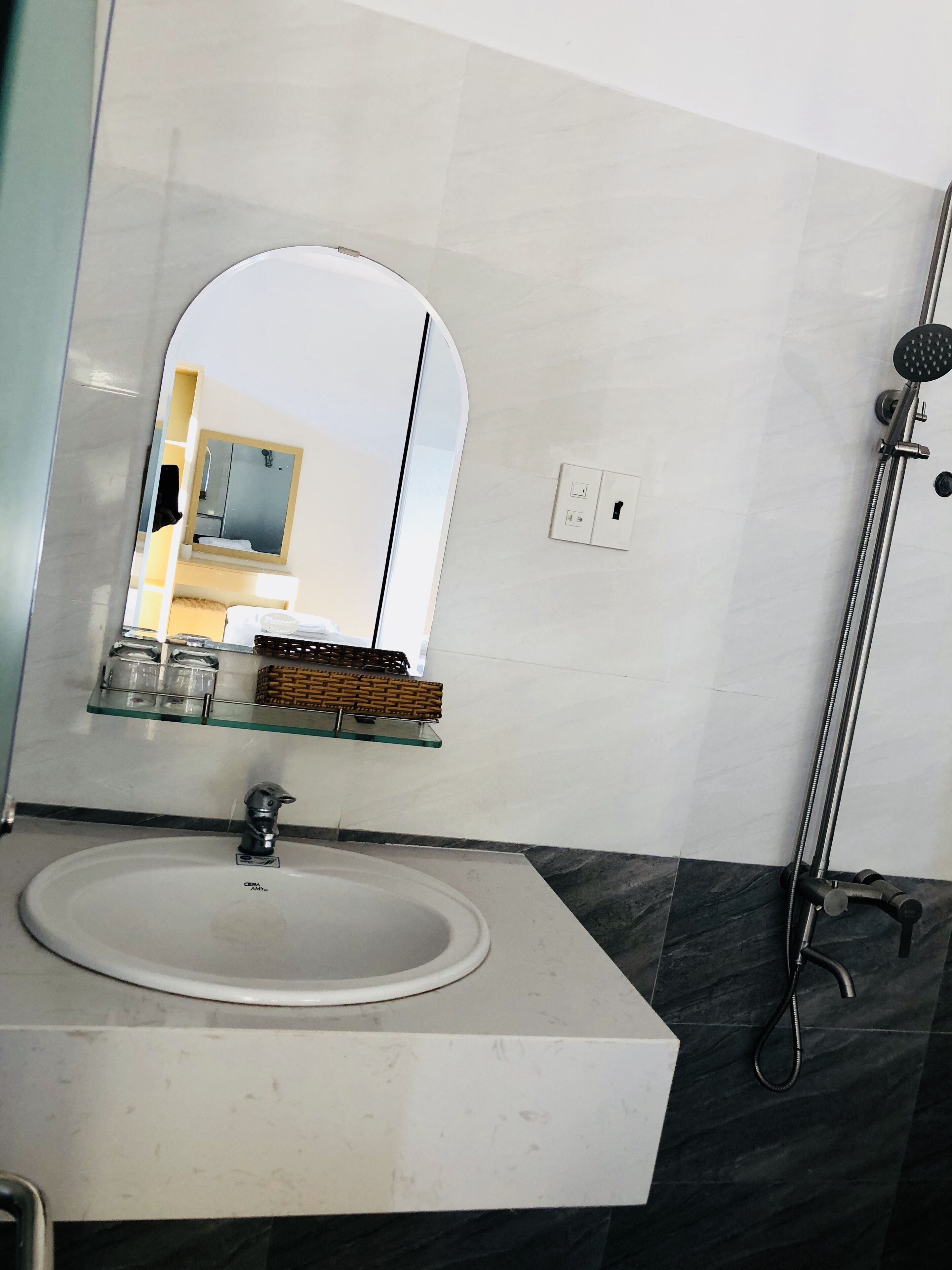 A bathroom with a white sink, a mirror, a shower, and a shelf with toiletries.