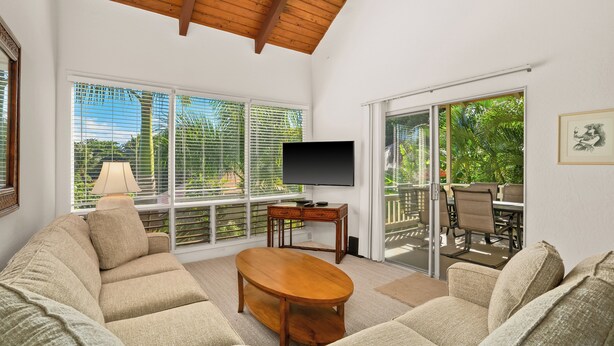 A living room with a sofa, a coffee table, a TV, and a balcony with outdoor furniture. - South Shore Island Getaway at Poipu Crater 7 (Po'ipu)