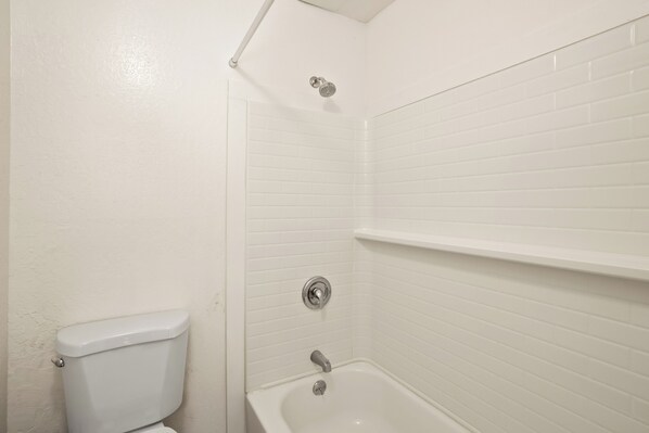 A bathroom with white tiled walls, a toilet, a bathtub, and a showerhead.