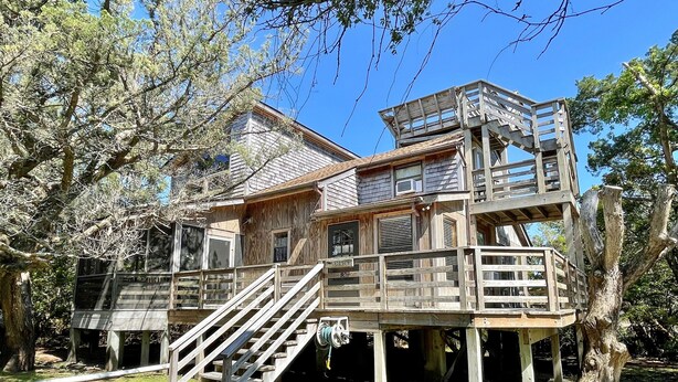 Una casa de madera con terraza y escaleras, rodeada de árboles.