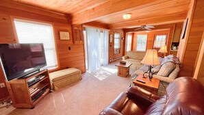 Una habitación acogedora de estilo cabaña con televisión, sofá de cuero y una mesa de comedor.
