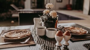 Une table dressée pour le petit-déjeuner, avec des crêpes, du café et des fleurs.