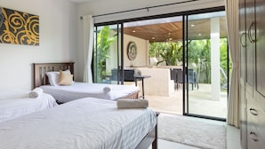 Une chambre d’hôtel avec deux lits, un bureau et une porte-fenêtre coulissante donnant sur une terrasse aménagée avec du mobilier d’extérieur.