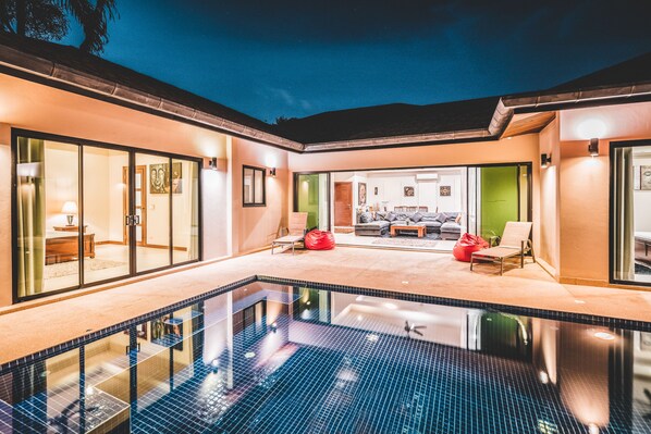 Ein Schwimmbad mit Glasüberdachung, eine Terrasse mit Sitzgelegenheiten und Blick ins Innere.